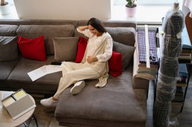 Hamile bir kadın rahatlama bölgesinde yumuşak yastıkların üzerine rahatça oturur. Rahat kıyafetler giyer.