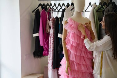 Gülümseyen tasarımcı pembe bir gece elbisesi yapar, işinde bir manken kullanır.