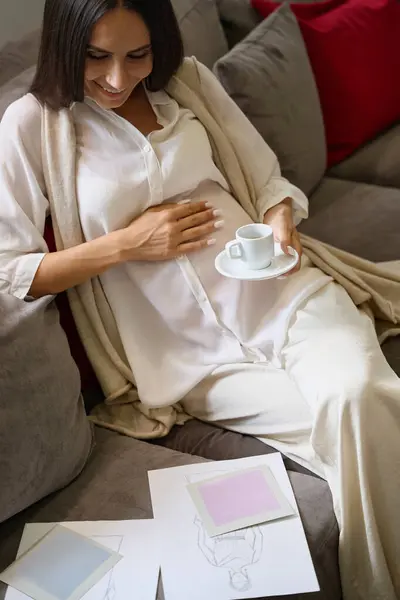 Lächelnde Schwangere Sitzt Auf Einem Sofa Mit Einer Tasse Kaffee — Stockfoto