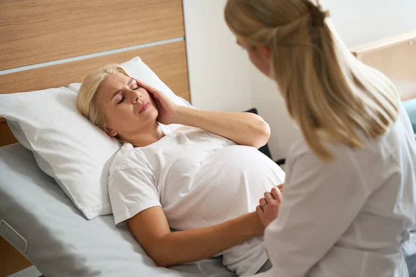 Krankenschwester Hält Erwachsene Kaukasische Schwangere Mit Kopfschmerzen Auf Medizinischem Bett — Stockfoto