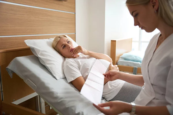 紧张的成年高加索孕妇躺在病床上 看着欧洲的女护士在产科医院检查她的心电图 — 图库照片
