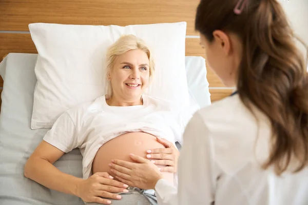 Lächelnde Europäerin Schaut Krankenschwester Die Ihren Schwangerschaftsbauch Der Geburtsklinik Überprüft — Stockfoto