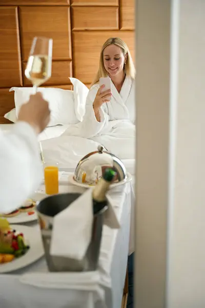 Młoda Kobieta Fotografująca Męża Szklanką Szampana Pokoju Hotelowym Śniadanie Serwowane — Zdjęcie stockowe