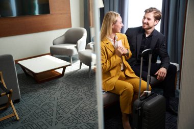 Mutlu çift bir otel odasına yerleşti, takım elbiseli ve bavullu insanlar.