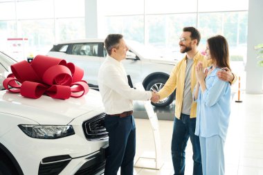 Manager congratulates the client with a handshake, the husband gives the car to his beloved wife clipart