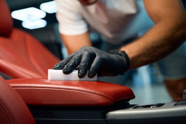 Koruyucu eldivenli bir adam deri bir kolluk temizler, melamine sünger kullanır.