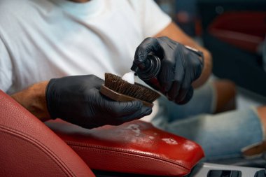 Adam fırçaya özel temizlik köpüğü sürüyor. Arabanın içini temizliyor..