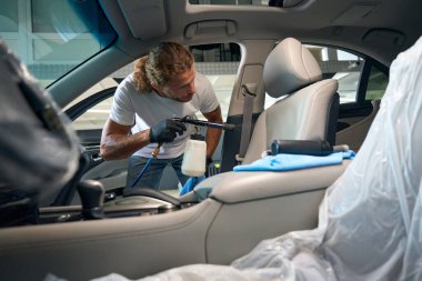 Uzun saçlı adam zarif bir arabanın ön koltuğunu temizliyor, modern bir tornador kullanıyor.