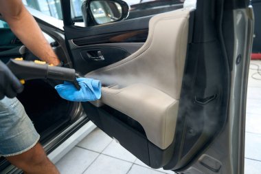 Adam zarif bir arabanın içindeki kiri kasırgayla temizliyor. Yumuşak mavi bir peçete kullanıyor.