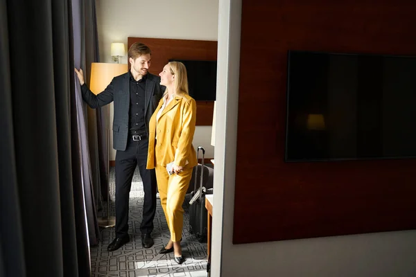 Happy travelers in travel suits stand by the window in a hotel room, the room has a minimalist interior