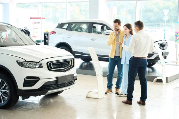 Nice couple in a car dealership communicates with a consultant, people choose a popular car model