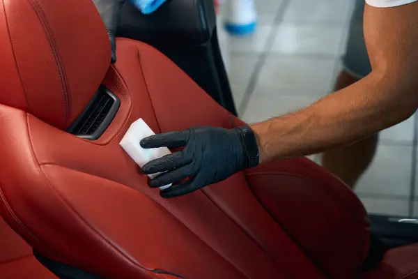 Cleaning a leather car seat with a melamine sponge, a man works in protective gloves