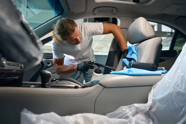 Traşsız adam zarif bir arabanın ön koltuğunu temizliyor, modern bir tornador kullanıyor.
