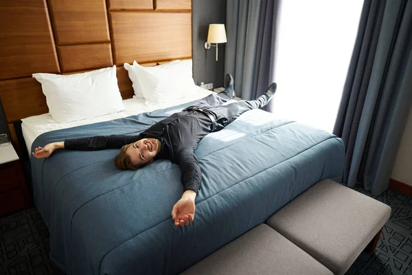 Handsome young man lies with his arms outstretched on a blue blanket, the room is clean and cozy
