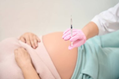 Beyaz bornoz ve güvenlik eldivenleriyle arka planda yatan sıvı, hamile bir kadın, Rh immünoglobülin enjeksiyonu, jinekoloji ve reprodükoloji.