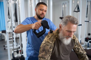 Doktor, rehabilitasyon sırasında bir askerin sırtına, kamuflaj kıyafeti giymiş bir hastaya donanım masajı yapar.