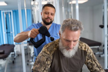 Uzman, rehabilitasyon sırasında bir askerin sırtına, kamuflaj kıyafeti giymiş bir hastaya donanım masajı yapıyor.