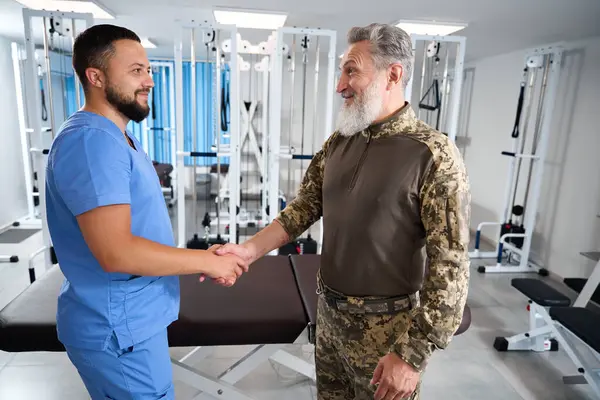 Chiropractor greets a man in military clothing at a rehabilitation center, the men shake hands