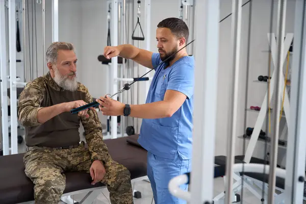 Rehabilitationstherapeut Hilft Einem Militärpatienten Bei Der Arbeit Einer Maschine Ein — Stockfoto