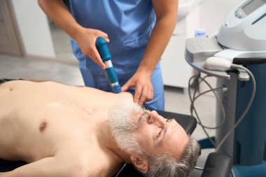 Rehabilitologist uses modern treatment methods for the patient, the man has a gray beard clipart