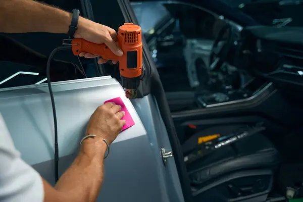 Powerful industrial dryer in the hands of a repairman, he is gluing anti-gravel film on car doors