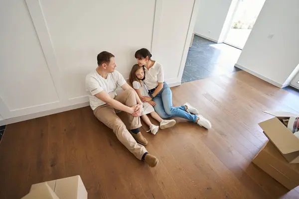 父親と母親がお互いを見つめあい 女性が娘を抱きしめ 引っ越し中に新しいタウンハウスの床に座っている 家族の将来の計画と関係 — ストック写真