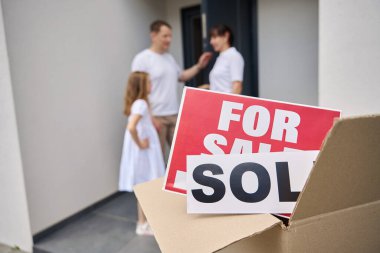 Ebeveynler ve kızları yeni evin verandasında duruyorlar, ön tarafta satılık tabelalarla dolu bir kutu var, satıldı.