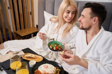 Genç sarışın kadın ve kocası rahat otel odasında kahvaltı yapıyorlar. Balayı süitinde kalıyorlar.