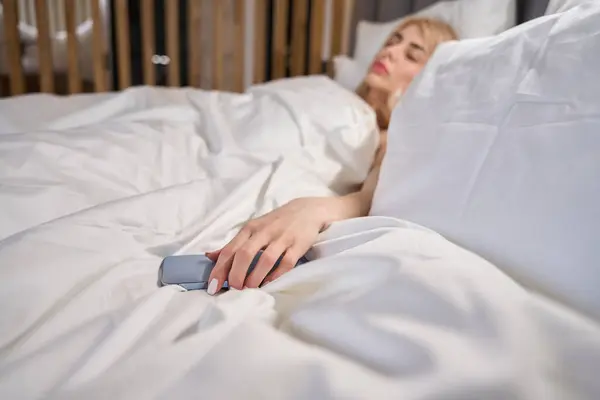 Sleeping blonde lies on fluffy pillows with a mobile phone, the bedroom is cozy