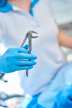 Koruyucu eldivenli diş hekimi, üniformalı bir doktorun dişlerini sökmek için bir alet tutuyor.