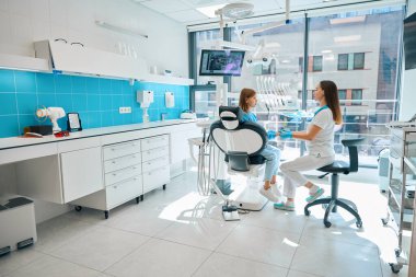 Diş hekimi genç bir hastayla dişçi muayenehanesinde iletişim kurar, doktor kızların elini tutar.