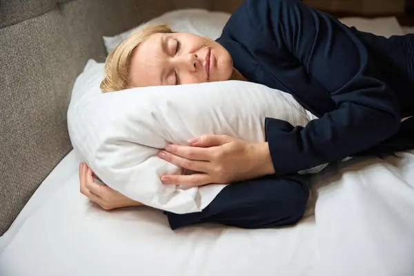 ベッドルームの居心地の良いベッドで柔らかい枕にナッピングスーツの女性起業家 — ストック写真