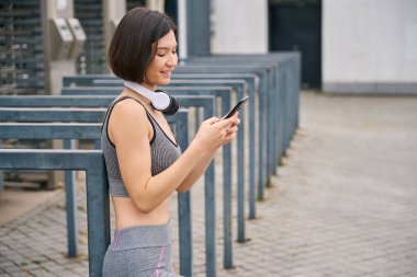 Kulaklıklı genç bir bayan elinde akıllı telefon ve sabah eğitimine hazırlanıyor. Spor anlayışı