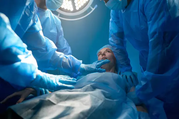 Woman patient waking up after surgery surrounded with professional medic team in operating room