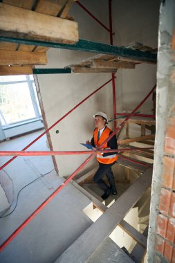 Bina müfettişi evi incelerken merdivenlerden çıkıyor ve elindeki panoya iliştirilmiş kağıtlara bir şeyler yazıyor.