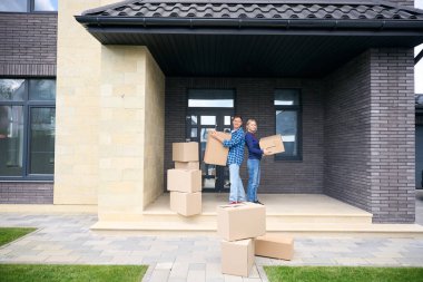 İçerik sahibi karı koca sırt sırta dururlar ve taşınma sırasında karton kutuları ellerinde tutarlar.