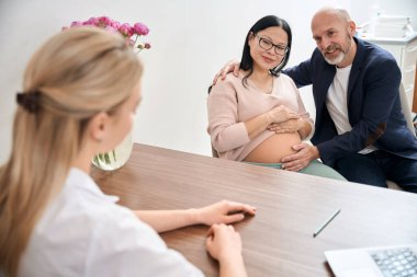 Yetişkin bir çift, hamileliğin üçüncü üç ayı ve onun yardımıyla bebek doğurma süreci hakkında konuşmak için kadın doğum muayenehanesine gidiyor.