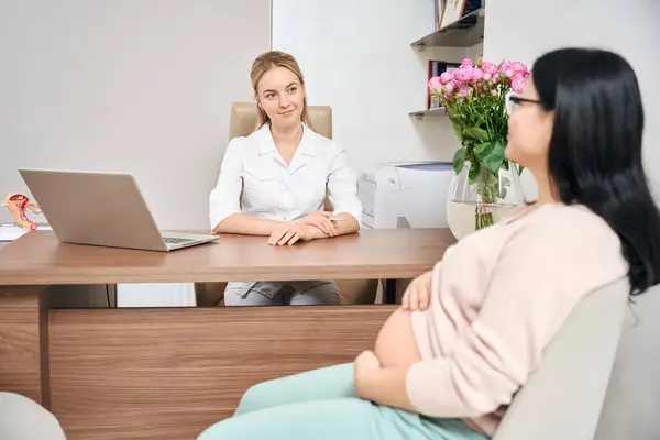 妊娠中の女性 若い婦人科医のオフィスに座って 彼女のホルモンと健康状態を共有し 赤ちゃんの配達プロセスについて尋ね 条件を議論 — ストック写真