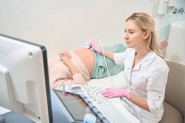 年轻合格的超声技师 为孕妇做超声检查 在腹部移动特殊的传感器 检查婴儿的健康和情况 妇科诊所 — 图库照片
