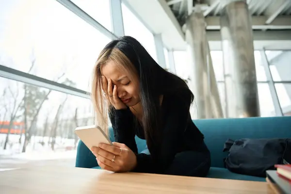 年轻的心烦意乱 哭哭啼啼的亚洲女性It员工在同事办公室的沙发上使用智能手机 现代自由职业或远程工作的概念 — 图库照片