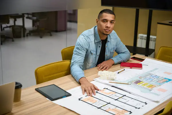 Copy space picture of sleepy african american guy sitting at table in office while working with building plan