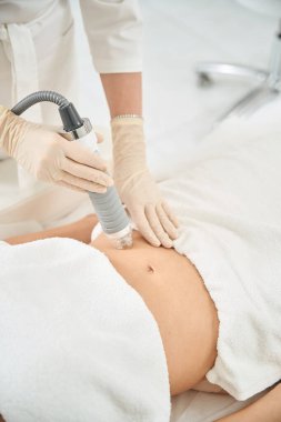 Yakın plan dermatokozmetik uzmanı hasta karnı, deri aktivasyonu ve hücre yenilenmesi, kolajen ve elastin üretimi, estetik ilaç kliniği üzerinde mikronedle ve radyo frekans terapisi taşıyor.