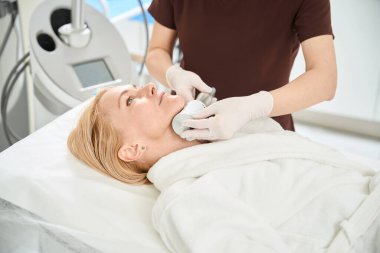 Estetik tıp kliniğinin profesyonel hemşiresi kadın hasta yüzüne son nokta terapisi uyguluyor. Genç elastin proteinleri ve cilt kolajeni üretimini teşvik ediyor.