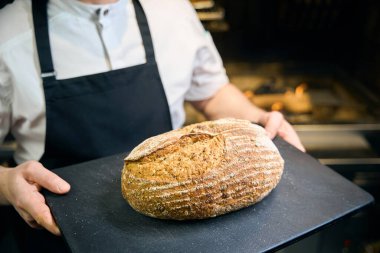 Kesilmiş erkek aşçı, restorandaki bulanık mutfakta ekmek dilimleme tahtası tutuyor. Lezzetli sağlıklı yemek kavramı