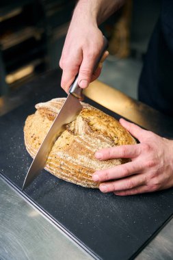 Kesilmiş erkek aşçı restorandaki bulanık mutfağın masasında bıçakla ekmek kesiyor. Lezzetli sağlıklı yemek kavramı