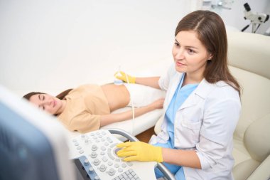 Kafkasyalı kadın jinekolog, modern klinikte doktora bakan Avrupalı genç bir kadının hamile karnının ultrason taramasını yapıyor. Hamilelik ve annelik kavramı