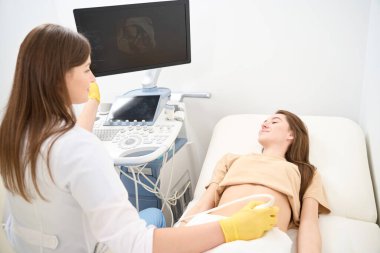 Beyaz kadın jinekolog, genç Avrupalı kadına hamile karın ultrasonu taramasının sonuçlarını modern klinikte gösteriyor. Hamilelik ve annelik kavramı