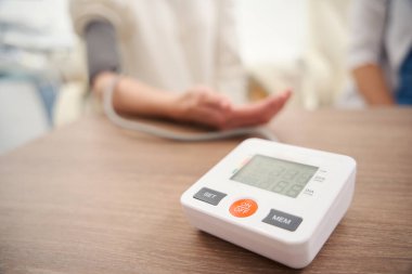 Kadın hasta klinikte doktorla kan basıncını ölçerken masadaki tonometrenin ön planına odaklan. Hamilelik ve annelik kavramı