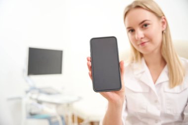 Klinikteki beyaz kadın jinekoloğun elindeki akıllı telefonun seçici odak noktası. Sağlık hizmetleri kavramı
