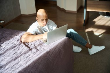 Yoğunlaşmış Afrikalı Amerikalı adam güneşli bir günde otel odasında dizüstü bilgisayar kullanıyor. Dinlenme, tatil ve seyahat kavramı